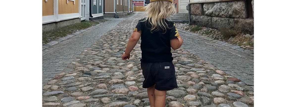 Pieni poika kävelee keskellä autotonta tietä mukulakivetyksellä paljain jaloin, Vanha Rauma.