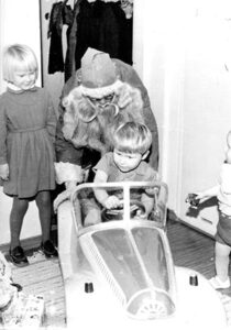 Joulupukki työntää polkuautoa ajavaa pikkupoikaa.