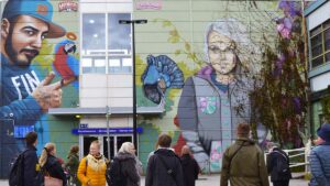 Ryhmä ihmisiä seisoo Myyrmäen asemalla olevan ison muraalin edessä. Muraalin tekijät: Salla Ikonen ja Mr. Dheo.