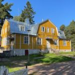 Keltainen seurantalo puutarhamaisessa ympäristössä.