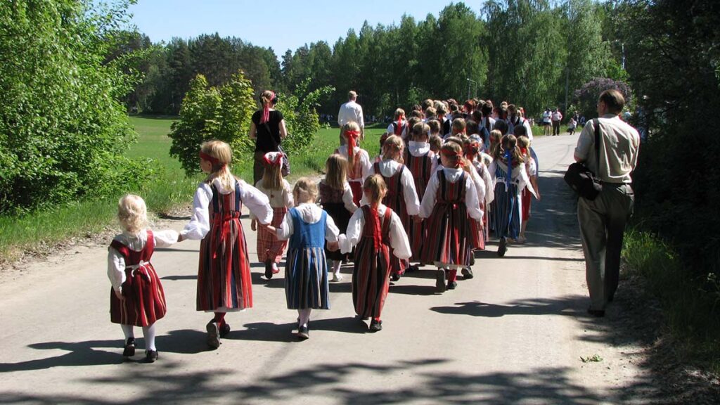Kansallispukuisia lapsia äänitetään, kun he kulkevat tietä pitkin.