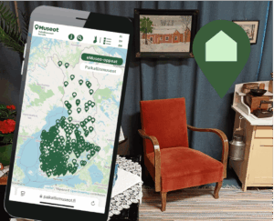 karttanäkymä puhelimen näytöllä ja taustalla nojatuoli sekä taulu