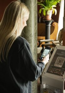 nainen skannaan puhelimella qr-koodia museossa