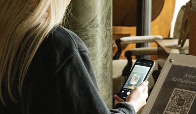 nainen skannaan puhelimella qr-koodia museossa