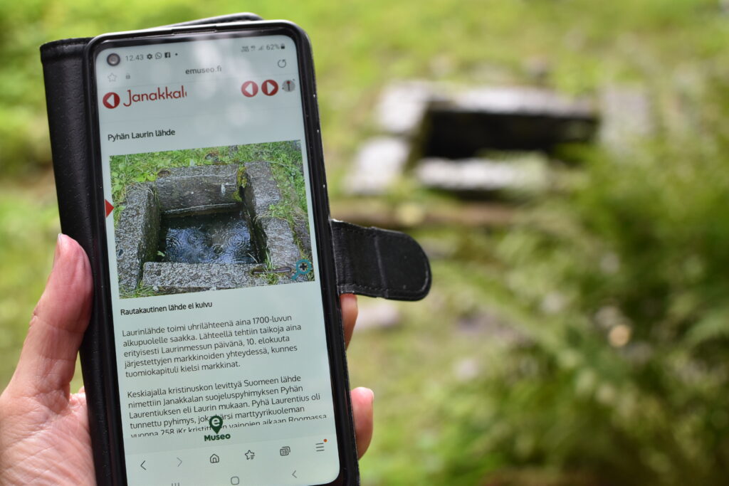 puhelin, jossa näkyy kivien ympäröimä lähde. Sama lähde kuvassa oikealla.