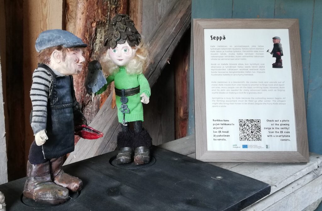 Nukkehahmot vasemmalla. Oikealla tekstitaulu, joka kertoo sepän ammatista.