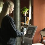 nainen tutkii museon opastaulun qr-koodia. Taustalla pylväs, viherkasvi, museon huonekaluja ja ikkuna