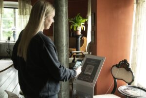 nainen tutkii museon opastaulun qr-koodia. Taustalla pylväs, viherkasvi, museon huonekaluja ja ikkuna