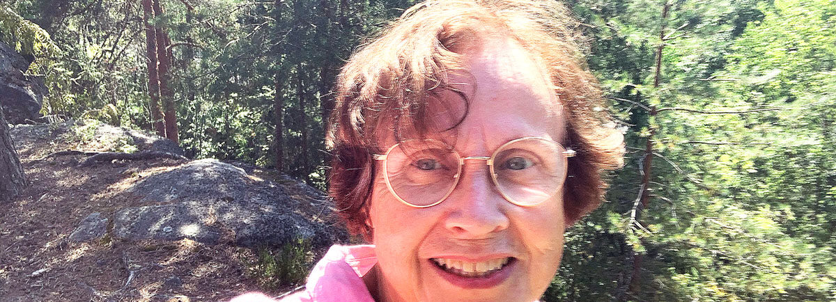 Virpi Hämeen-Anttila kirkkaana kesäpäivänä, taustalla kalliota ja mäntymetsää.