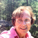 Virpi Hämeen-Anttila kirkkaana kesäpäivänä, taustalla kalliota ja mäntymetsää.