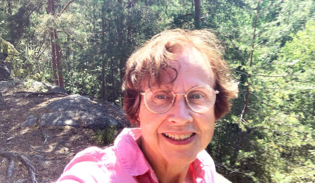 Virpi Hämeen-Anttila kirkkaana kesäpäivänä, taustalla kalliota ja mäntymetsää.