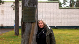 Eeva Snellman nojaa kelopuuhun, johon on kiinnitetty kyltti. Teos on pystytetty Sodankylän vapauttamisen 20.10.1944 vuosipäivänä 1974.