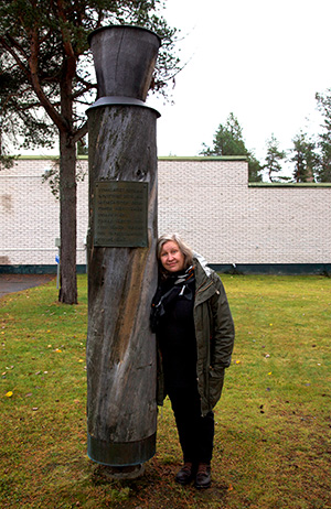 Eeva Snellman nojaa kelopuiseen seitaan, johon on kiinnitetty kyltti. Teos on pystytetty Sodankylän vapauttamisen 20.10.1944 vuosipäivänä 1974.