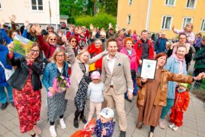 Riemuitsevia monenikäisiä ihmisiä Kumpulassa, Helsingissä, taustalla kerrostaloja.