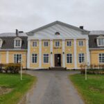 Keltainen suuri seurantalo puutarhamaisessa ympäristössä.