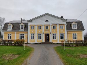 Keltainen suuri seurantalo puutarhamaisessa ympäristössä.