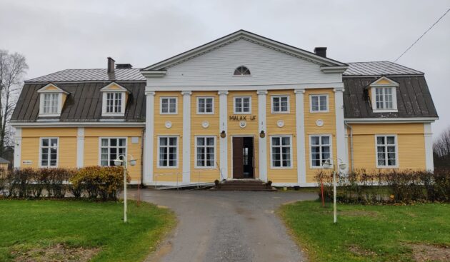 Keltainen suuri seurantalo puutarhamaisessa ympäristössä.