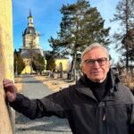 Erkki Taskila nojaa vanhaan rakennukseen. Taustalla on kirkon torni.