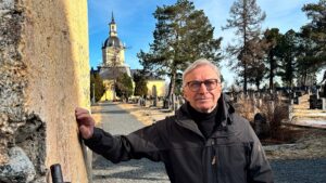Erkki Taskila nojaa vanhaan rakennukseen. Taustalla on kirkon torni.