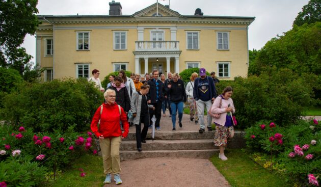 Keltaisen kartanorakennuksen edessä iso joukko ihmisiä.