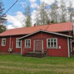 Punainen seurantalo, jonka edessä nurmikkoa ja takana koivuja