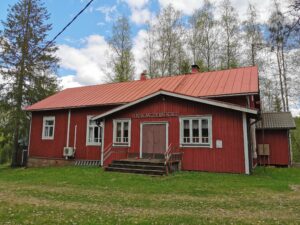 Punainen seurantalo, jonka edessä nurmikkoa ja takana koivuja