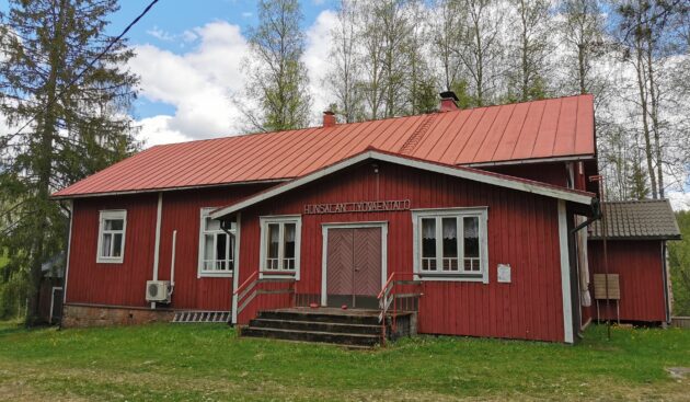 Punainen seurantalo, jonka edessä nurmikkoa ja takana koivuja